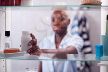 View Through Bathroom Cabinet Of Young Woman Taking Medication From Container