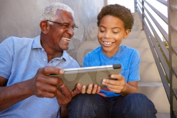 Close Up Of Grandfather With Grandson Sitting On Steps Outdoors At Home Using Digital Tablet