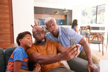 Multi-Generation Male African American Family On Sofa At Home Posing For Selfie On Mobile Phone
