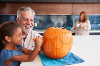 Granddaughter With Grandparents Carving Halloween Lantern From Pumpkin At Home