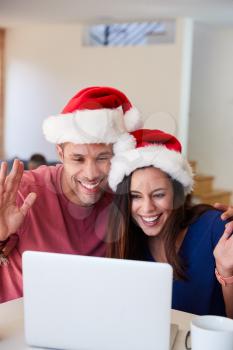 Hispanic Couple Wearing Santa Hats With Laptop Having Video Chat With Family At Christmas