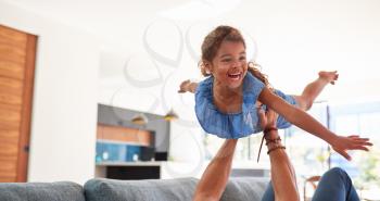 Father Playing Game With Daughter Lying On Sofa And Lifting Her In The Air