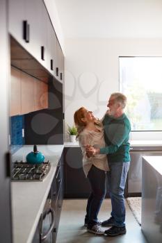 Senior Hispanic Couple At Home Dancing In Kitchen Together