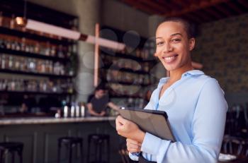 Portrait Of Confident Female Owner Of Restaurant Bar Standing By Counter Holding Digital Tablet