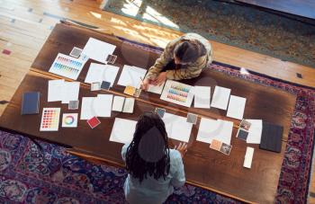 Overhead View Of Two Women Having Creative Design Meeting Around Wooden Table In Office