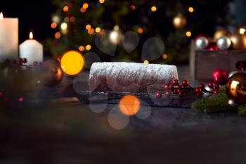 Traditional Yule Log On Table Set For Festive Christmas Meal With Tree Lights In Background