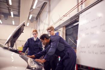 Male Tutor With Students Looking At Car Engine On Auto Mechanic Apprenticeship Course At College