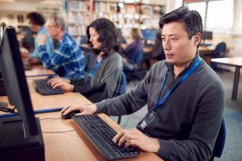 Group Of Mature Adult Students In Class Working At Computers In College Library