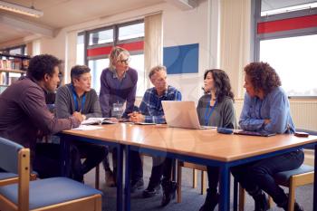 Teacher With Group Of Mature Adult Students In Class Sit Around Table And Work In College Library