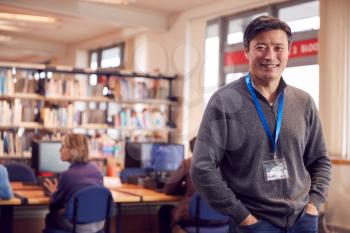 Portrait Of Mature Male Teacher Or Student In Library With Other Students Studying In Background