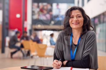 Portrait Of Mature Female Teacher Or Student With Digital Tablet Working At Table In College Hall