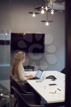 Businesswoman Working Late In Office Meeting Room Using Laptop