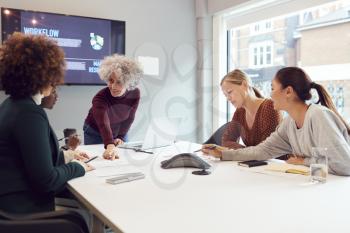 Mature Businesswoman Leading Creative Meeting Of Women Collaborating Around Table In Modern Office