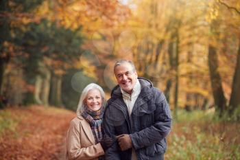 Portrait Of Loving Senior Couple Walking Along Autumn Woodland Path Through Trees