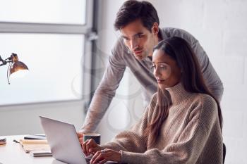 Businesswoman Working On Laptop At Desk Collaborating With Male Colleague