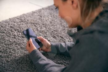 Overhead Shot Of Woman Looking At Screen With Copy Space On Mobile Phone Lying On Carpet