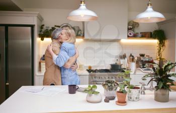 Loving Mature Couple Hugging As They Look At Financial Paperwork In Kitchen At Home