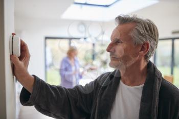 Mature Man Turning Control Dial On Digital Central Heating Thermostat At Home