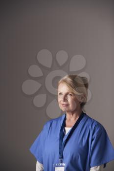 Studio Portrait Of Mature Female Nurse Wearing Scrubs Standing Against Grey Background