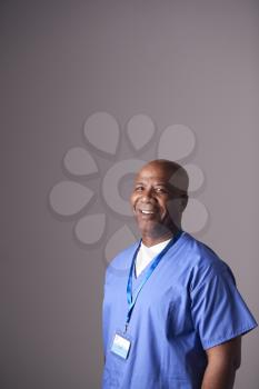 Studio Portrait Of Male Nurse Wearing Scrubs Standing Against Grey Background