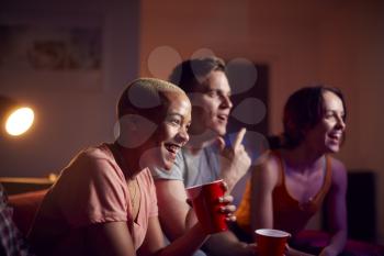 Group Of Friends With Drinks Sitting On Sofa At Home Watching Movie Together