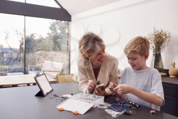 Grandson With Grandmother Assembling Electronic Components To Build Robot Together At Home