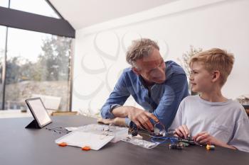 Grandson With Grandfather Assembling Electronic Components To Build Robot Together At Home