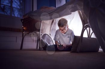 Boy Sitting In Den Or Camp He Has Made At Home Playing With Mobile Phone