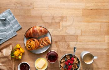 Overhead Flat Lay Shot Of Table Laid For Breakfast With Cereal Croissant Pastries And Flowers