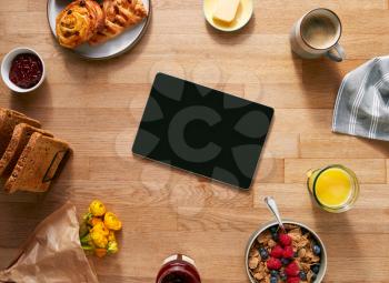 Overhead Flat Lay Of Digital Tablet On Table Laid For Breakfast With Cereal Croissant And Flowers