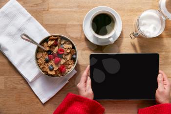 Overhead Flat Lay Of Woman Using Digital Tablet On Table Laid For Breakfast With Cereal And Coffee