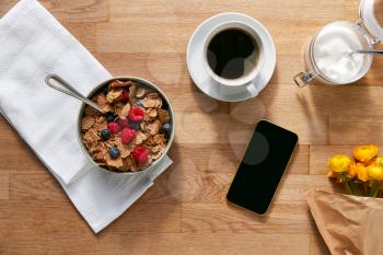 Overhead Flat Lay Of Mobile Phone On Table Laid For Breakfast With Cereal And Coffee