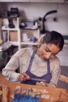 Female Jeweller At Bench Working On Ring With File In Studio