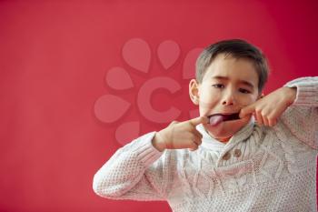 Portrait Of Young Boy Against Red Studio Background Pulling Funny Faces At Camera