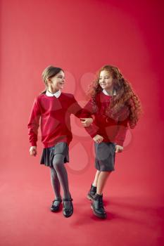 Two Elementary School Pupils Wearing Uniform Linking Arms Against Red Studio Background