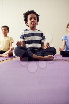 Group Of Children Sitting On Exercise Mats And Meditating In Yoga Studio