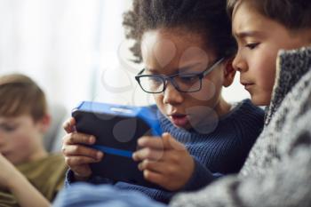 Group Of Young Boys Gaming Together On Hand Held Devices At Home