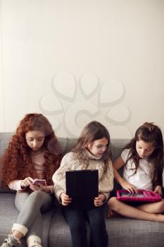 Group Of Girls With Friends Sitting On Sofa At Home Playing On Digital Tablet And Mobile Phones