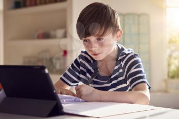 Boy Sitting At Kitchen Counter Doing Homework Using Digital Tablet