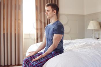 Man Sitting On Edge Of Bed At Home Meditating During Lockdown For Covid-19