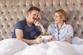 Couple Eating Strawberries For Breakfast In Bed To Celebrate Wedding Anniversary