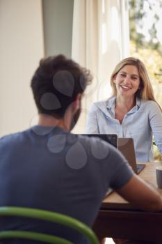 Couple With Laptop Sitting At Table Working From Home Together
