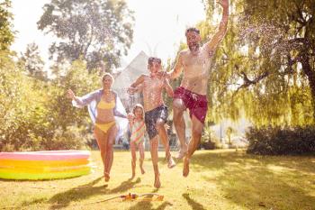 Family Running Through Water From Garden Sprinkler Having Fun Wearing Swimming Costumes