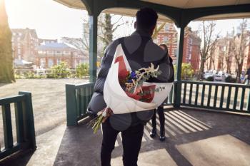 Romantic Man With Bouquet Of Flowers Behind Back Surprising Young Woman As They Meet In City Park