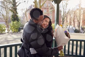Romantic Man Hugging Young Woman After Giving Her Bouquet Of Flowers As They Meet In City Park