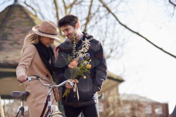 Woman With Bike Meets Man Holding Flowers On Date In City Park