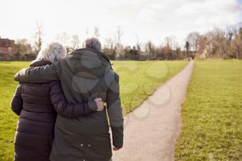 Rear View Of Loving Senior Couple Enjoying Autumn Or Winter Walk Through Park Together