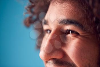 Close Up On Eyes Of Smiling Young Man Against Blue Background In Studio