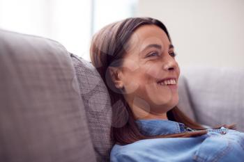 Smiling Young Woman At Home Lying On Sofa Watching TV And Laughing