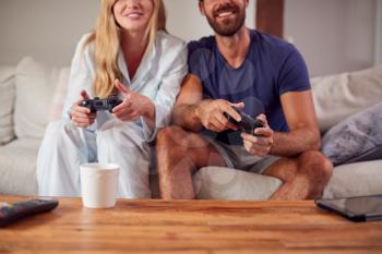 Couple Wearing Pyjamas Sitting On Sofa Playing Computer Game Together